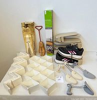 Photo showing white plastic drawer divider panels interlocked to form 32 compartments laid flat, wooden shoe stretcher with handle in original box, plastic shoe stackers, adjustable shoe trees in grey and beige, and a pair of shoes (not included).