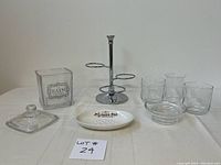 Full set of decorative bathroom vanity items laid out on a white cloth, showing glass jar with lid, chrome three-tier bath caddy with glass components, two extra glass cups, and white ceramic soap dish.
