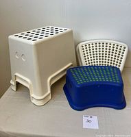 Four assorted size plastic step stools; two tall white rectangular, one medium white curved, one medium blue curved, all with perforated tops.