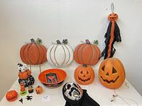 Full view of Halloween decor including the three metal yard stake pumpkins, hanging Jack O Lantern with streamers, triple tier stuffed pumpkin stack, large plastic Jack O Lantern candy bowl, small Halloween figurines and decorations.
