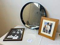 Front view of the navy blue round mirror and three different picture frames on a white table