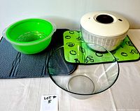 Oxo salad spinner, green fruit wash basin, glass salad bowl, green and grey drying mats displayed on a table