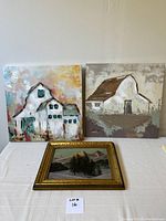 Front view of two folk art style acrylic canvas paintings featuring barn and farmhouse, displayed behind smaller framed mountain scene painting on table.