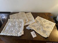 Four cream shantung silk pillowcases on wooden surface showing ornate beaded and sequin floral patterns.