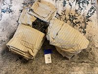 Photo of the four beige striped cotton sheets and pillowcases spread on a textured rug, showing the fabric's smooth striped pattern and neutral color.