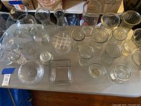 Photo showing a large variety of clear glass vases in different shapes and sizes on a table.