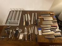 Overview of the lot showing knives, cleavers, kitchen utensils, and drawer organizers spread on a wooden surface.