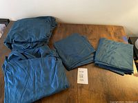 Dark teal king size sheet set including fitted sheet, top sheet, and two pillowcases folded on a wooden surface.
