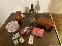 Photo showing Lane cedar box with key, green bubbling beaker with skull design, brown ceramic owl, floral patterned dish, pink decorative box, vintage matchboxes, small photo card, and fabric bundle on wooden table.