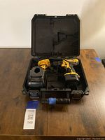 Open black plastic DeWalt carrying case with cordless drill, charger, and two batteries inside