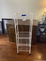 Front and side view of white metal exercise equipment rolling rack with multiple shelves and hooks for holding workout accessories. Rack is on caster wheels.