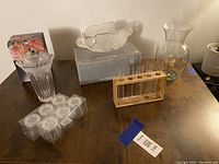 Photo showing multiple glass decor items: leaf-shaped glass bowl on top of a box, clear glass bulbous vase, wooden propagation station with six glass test tubes, and packaged small clear plastic jars.
