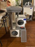 Full view of gray cat tree with cubby holes, scratching posts, a removable bed on top, and cat toy on the platform.