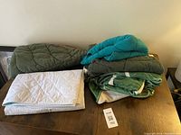 Five leaf-themed items arranged on table including two large leaf-shaped blankets, two padded leaf-shaped pillows in teal and green, and a white quilted waterproof pad.