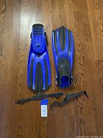 Top view of the pair of blue Mares scuba fins laid on wooden floor, with two black adjustable heel straps placed separately next to the fins.