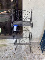 Front view of a small black metal shelf with decorative fan-shaped back and perforated top shelf.