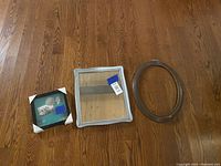 Photo showing three items: a small black square photo frame with glass and white corner protectors, a square silver mirror with glass, and an oval silver decorative frame without glass.