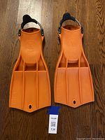 Top view of the pair of bright orange RK3 fins with spring straps on wooden floor.