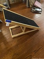 Side angled view of the adjustable wooden pet ramp showing the black carpeted surface and the wooden support structure underneath.