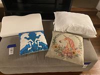 Photo showing three bed pillows and two unicorn themed throw pillows on a grey surface.