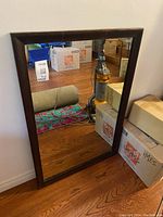 Full view of the rectangular mirror showing the dark wood frame and reflective surface in a room setting with some surrounding objects.