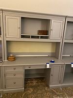 Front view of grey Stanley desk with hutch attached, showing closed cabinet doors and drawer fronts, along with open center shelf area.
