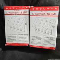 Two boxed Acolyte Nu-tek E-WallWash 12 SMT LED light fixtures with product diagrams and details on boxes