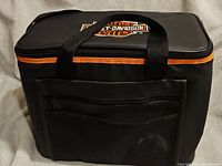 Front angle of the black Harley-Davidson cooler bag showing front zippered pocket, mesh pocket, handles, and orange zipper accent.