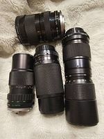 Four assorted black manual camera lenses laid out on fabric, showing different sizes, grips, and mount ends.