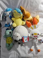 Full view of 7 assorted Pokémon plush toys including Glaceon, Cyndaquil, Eevee, Squirtle, Wooloo, and Scorbunny