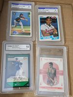 Photo showing four graded sports cards including Dennis Eckersley graded 9, Dave Justice graded 8, Ryan Braun graded 10, and Michael Phelps graded 10.