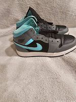 Side profile of the pair showing aqua Nike swoosh, grey and black leather, aqua collar, and white midsole.