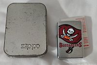 Zippo lighter with Tampa Bay Buccaneers logo alongside metal Zippo case with embossed branding.