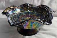 Side angle showing the iridescent finish, ruffled edge, and pedestal base on the black carnival glass bowl.