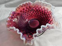 Angled side view showing the deep ruby hobnail pattern and the ruffled opaque opalescent rim
