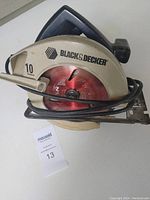 Front side of the Black & Decker circular skill saw showing the blade guard, red circular blade, handle, and cord wrapped around the tool.