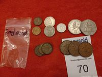 Coins laid out on red fabric with small plastic bag marked England to left