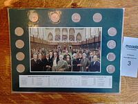 Top view of the green mounting board displaying the 12 Canada 125 quarters arranged around a central photograph of Canadian Prime Ministers from 1867 to 1967. Shows all coins and the image clearly.