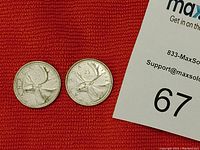 Two Canadian 25 cent coins lying on a red textured surface, adjacent to a MaxSold bid card.