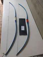 Two classic style longbows with blue limbs and different colored grip wraps, displayed on a white surface alongside a piece of paper with auction lot number.