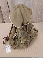 Photo showing front view of the green canvas knapsack with flap cover and leather straps spread out on a surface.