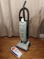 Front view of Dirt Devil upright vacuum cleaner with vacuum bags on the floor in front of it.