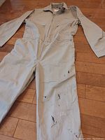 Full view of beige coveralls laid flat showing front zipper, collar, sleeves and stained areas on legs.