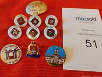 Photo showing all 9 pins laid out on orange background with maxsold paper including taxi badge, six Kingston Canada pins, Kingston Police Force pin, Kingston City Hall pin and 1978 Winter Games pin.