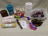 Various yarn spools, yarn rolls, a bag of yarn remnants and embroidery threads laid out on a beige fabric surface.