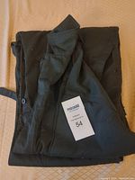 Folded coveralls with size tag '54' on top indicating size medium-large, dark green fabric visible.