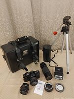 Complete lot displayed with camera body, lenses, flash, tripod, case, and accessories on beige surface.