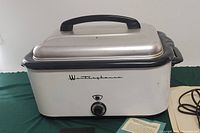 Front and side view of large vintage Westinghouse electric roaster oven with lid, temperature dial and black trim on green cloth background.