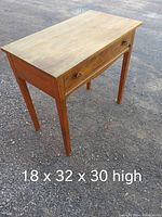 Full view of the wooden desk showcasing top, legs, and drawer with floral knobs, placed outdoors on gravel surface.