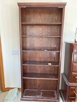 First dark wood bookcase shown from front, five shelves visible with slight wear and dust on shelves.